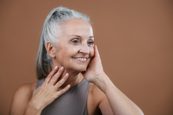 Studio portrait of beautiful senior woman with long gray hair holding her face. Isolated on a brown pink background. Copy space.