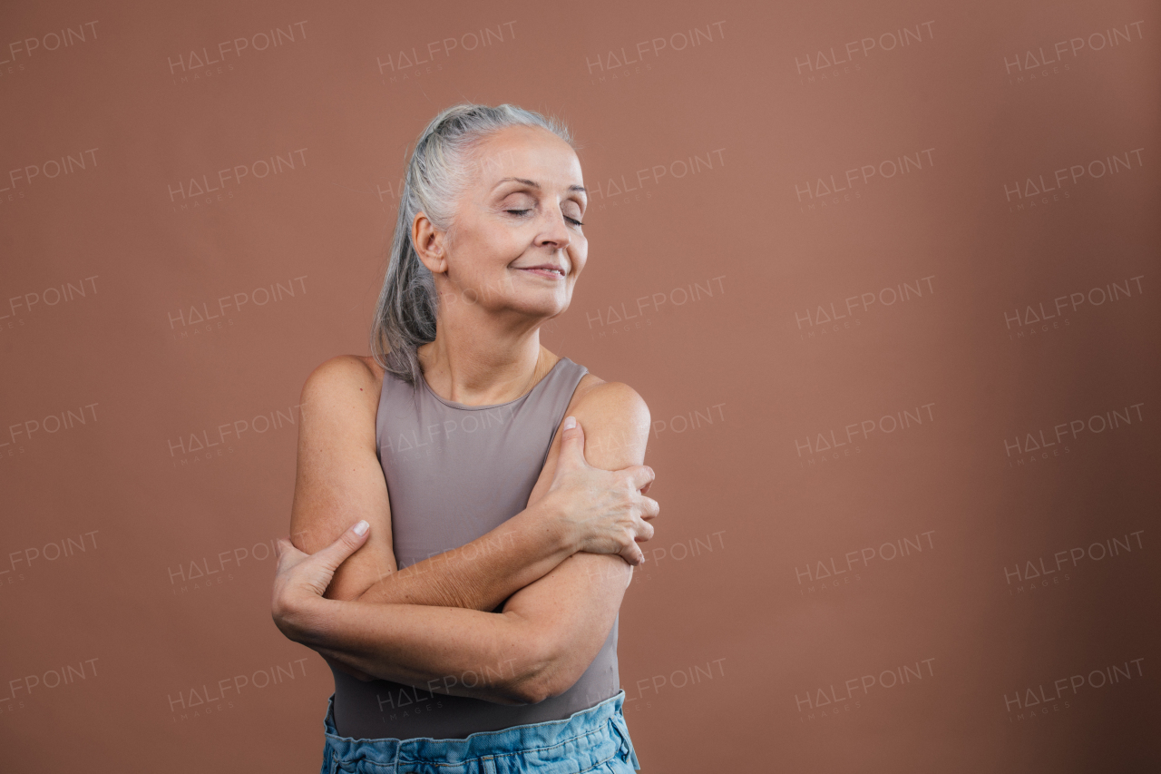 Studio portrait of beautiful senior woman with long gray hair and closed eyes. Isolated on a brown pink background. Copy space.