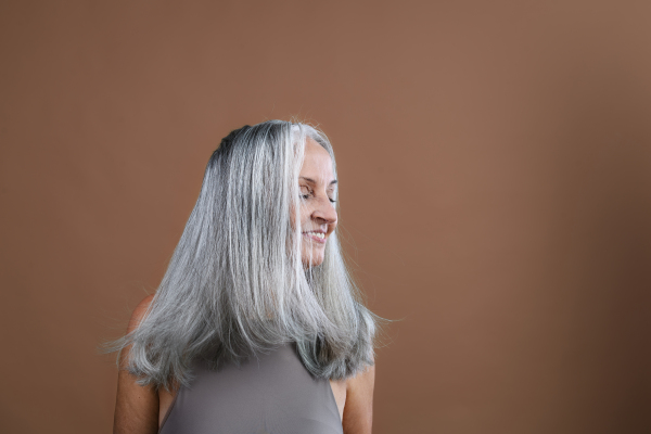 Side view of beautiful senior woman with long thick gray hair. Isolated on a brown pink background. Copy space.