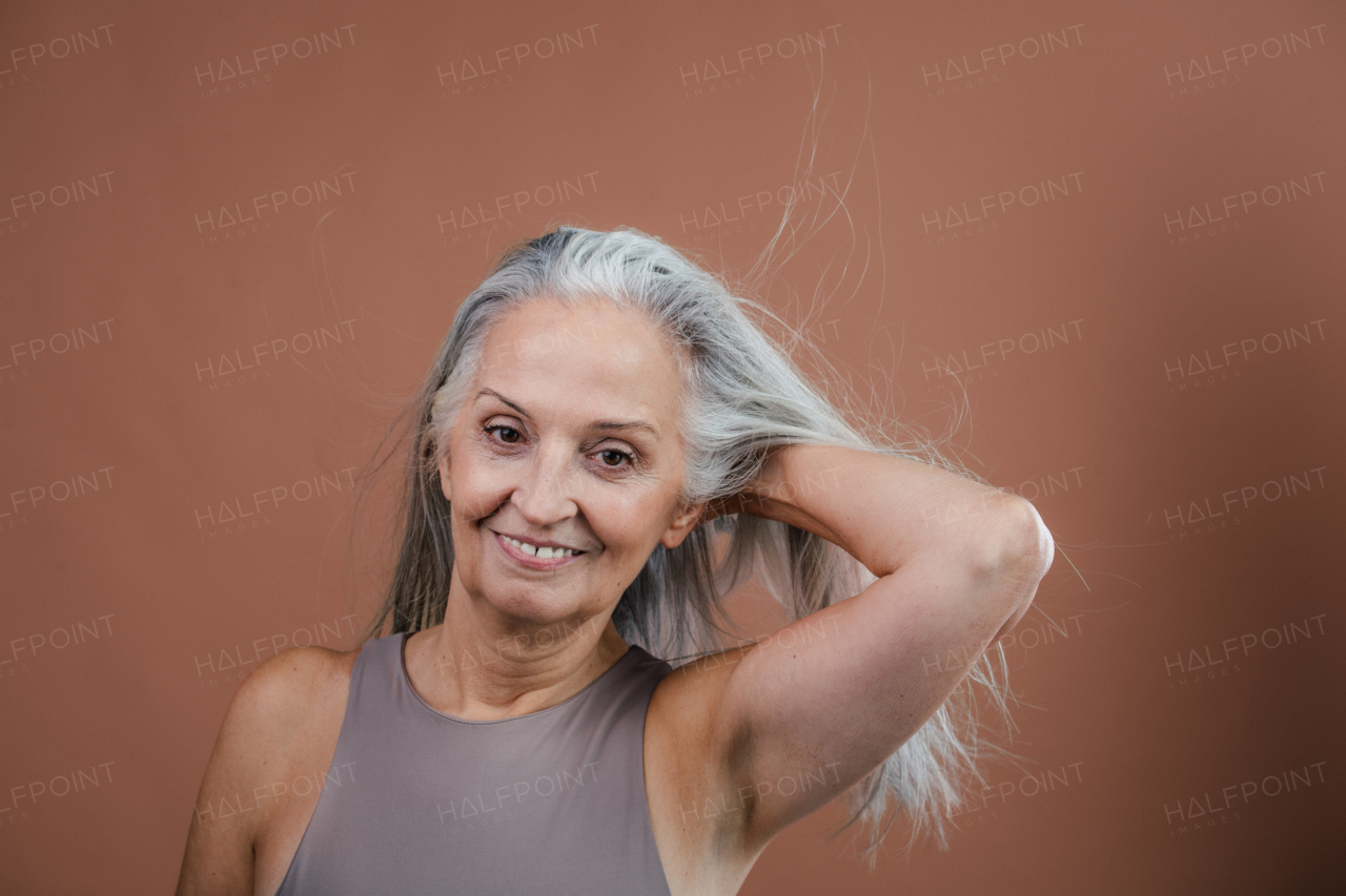 Studio portrait of beautiful senior woman holding her long gray hair. Isolated on a brown pink background. Copy space.