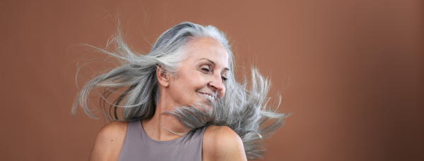 Side view of beautiful senior woman tossing her long thick gray hair. Isolated on a brown pink background. Banner with copy space.