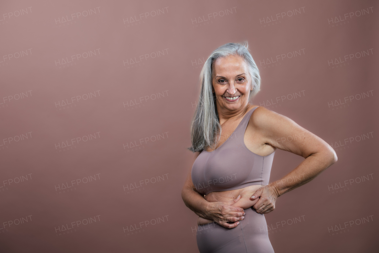 Portrait of senior woman in a lingerie, studio shoot. Beautiful body shape of aging woman. Isolated on a brown pink background. Copy space.