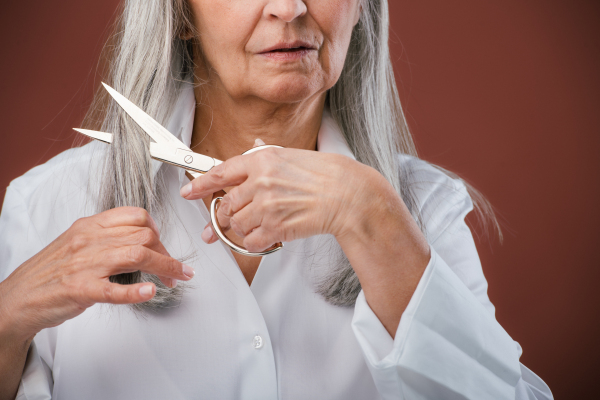 Portrait of unhappy senior woman cutting her hair because of breast cancer. Breast cancer awareness concept.