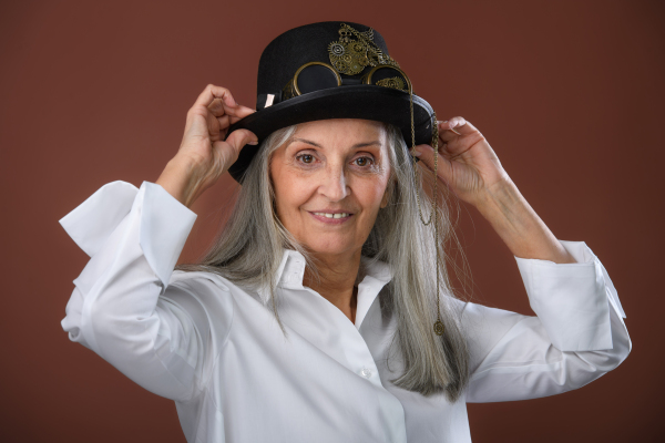 Portrait of happy senior woman in a shirt and hat, studio shoot.