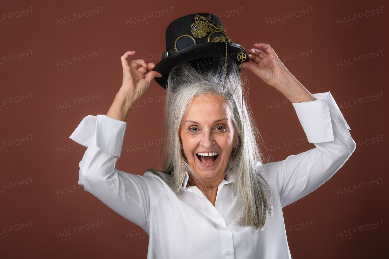 Portrait of happy senior woman in a shirt putting hat on her head, studio shoot.