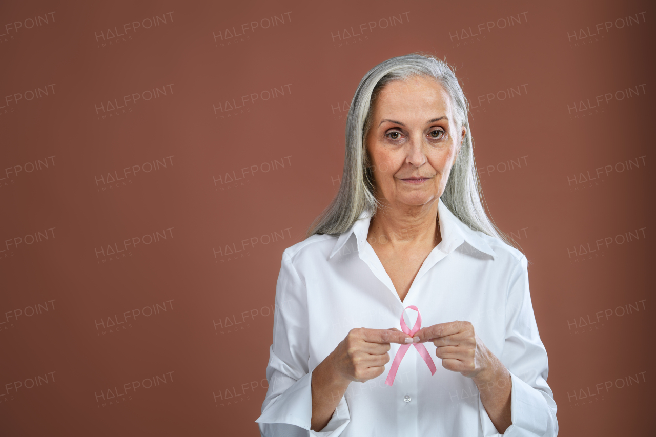 Senior woman holding the pink bow. Breast cancer awareness concept.