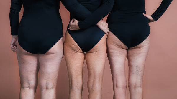 Rear view of three senior friends holding each other, body positivity concept. Beautiful body shape of aging woman, signs of age on woman body. Isolated on pink brown background.