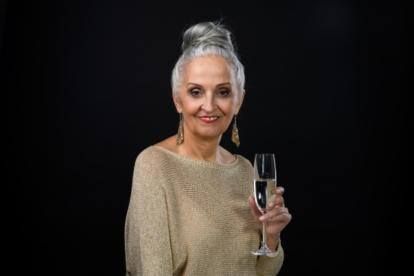 Portrait of well dressed senior woman in party outfit holding glass of champagne, Celebration concept. Isolated on black background.