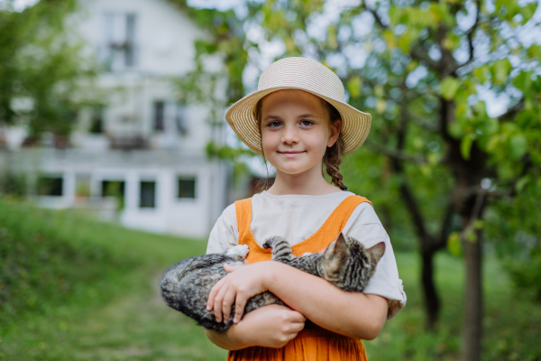 Portrait of a cute little girl in an autumn garden holding cat in the arms.