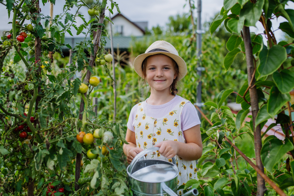 Portrait of a cute young girl watering plants with watering can in a field.