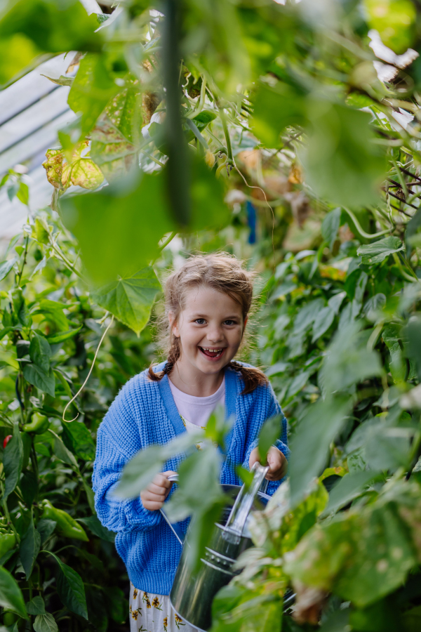 Portrait of a cute young girl standing in a greenhouse in the middle of growing vegetables.