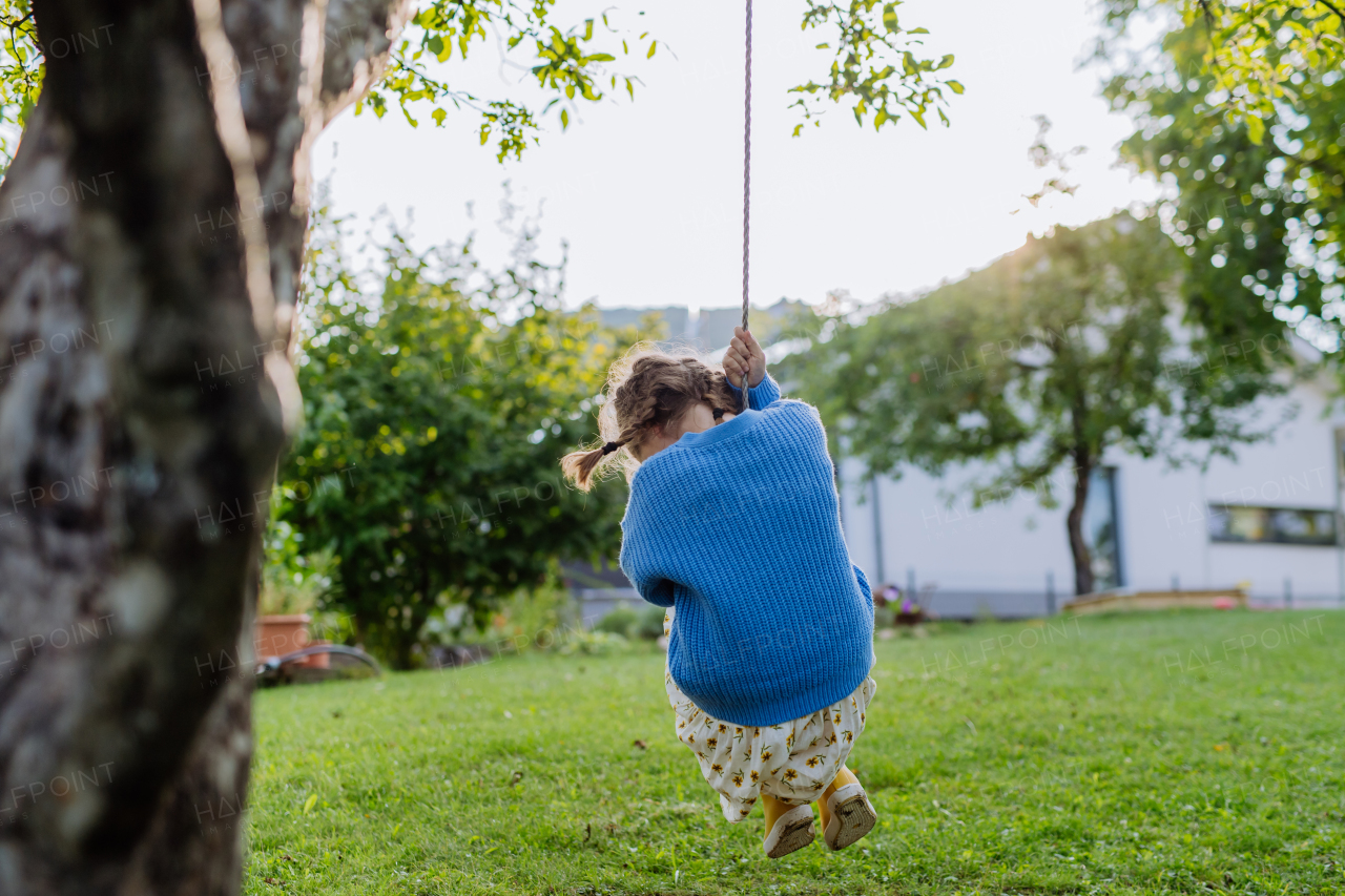 A young girl swinging on a swing in the garden. The schoolgirl spending free time with her grandparents in the garden on a warm autumn day.