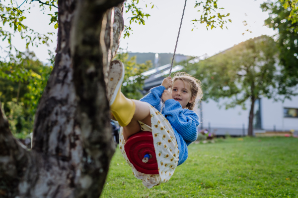 A young girl swinging on a swing in the garden. The schoolgirl spending free time with her grandparents in the garden on a warm autumn day.