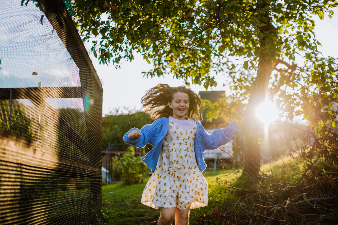 Cute girl running through her grandparents' garden during a warm autumn evening.