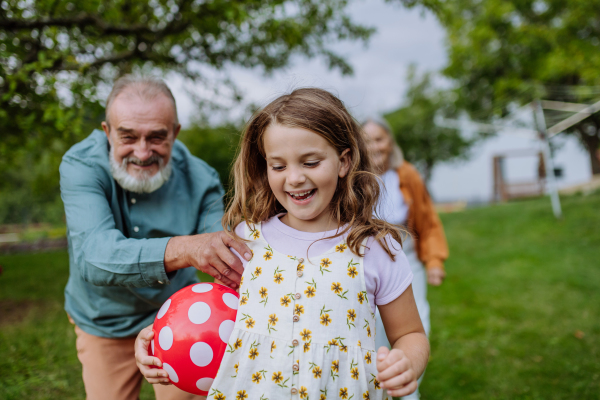 Grandparents playing with their grandchildren in the garden, tossing a ball having fun during warm autumn day.