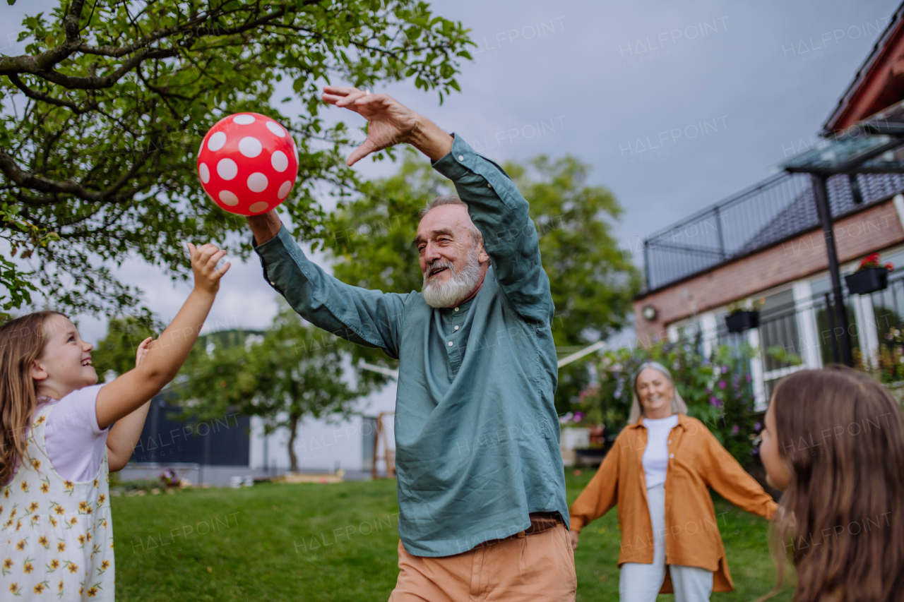 Grandparents playing with their grandchildren in the garden, tossing a ball having fun during warm autumn day.