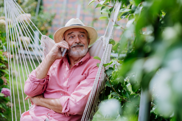 Happy senior sitting in a garden swing and phoneing.