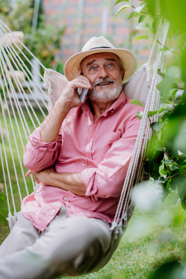 Happy senior sitting in a garden swing and phoneing.