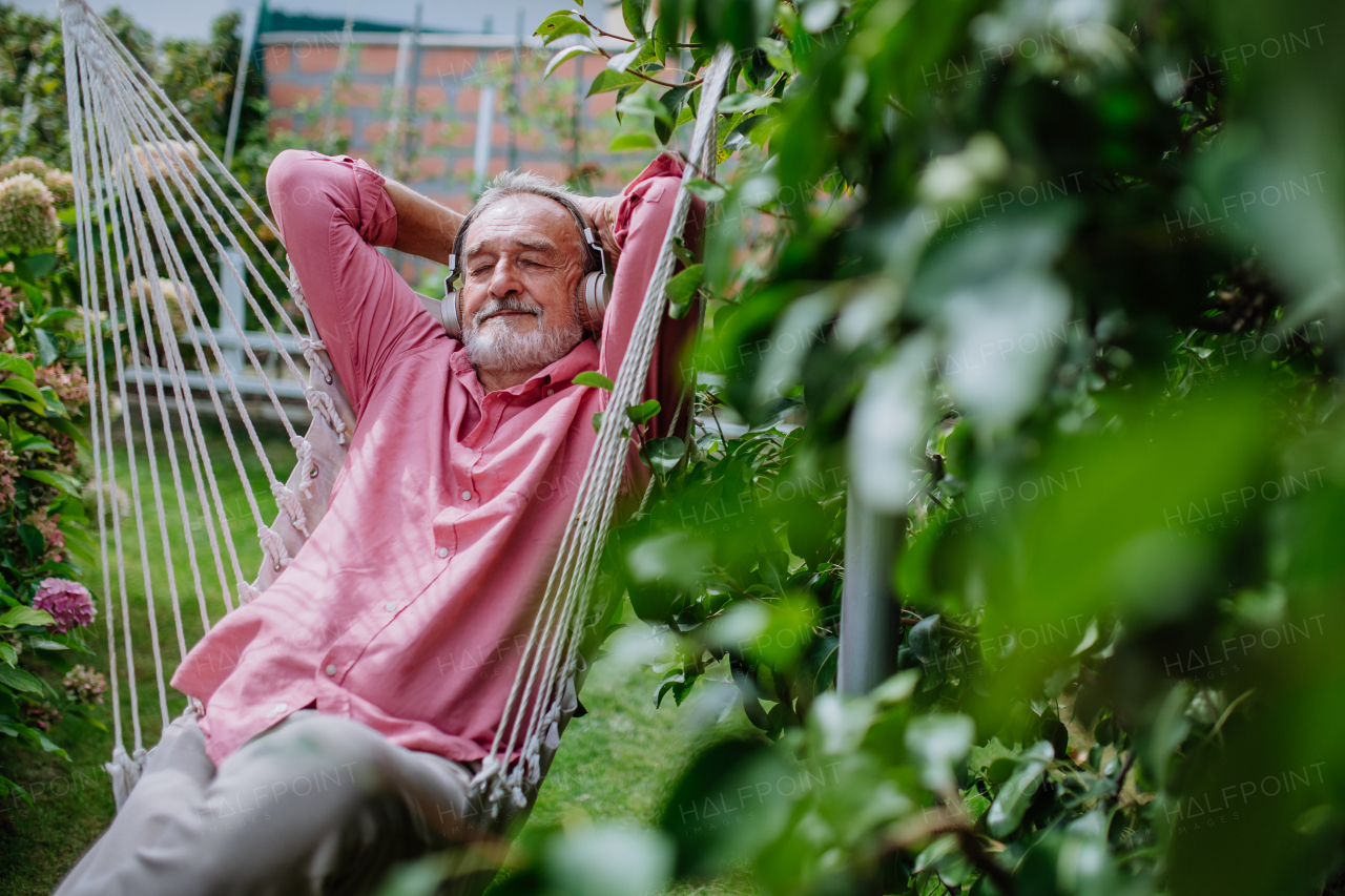 Happy senior man listening music and relaxing in outdoor swing,in a garden.