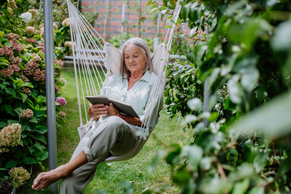 Senior woman relaxing in garden swing with a book.