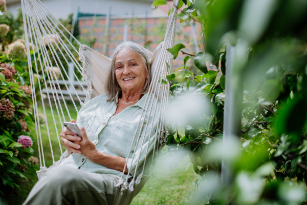 Senior woman relaxing in garden swing with a smartphone.