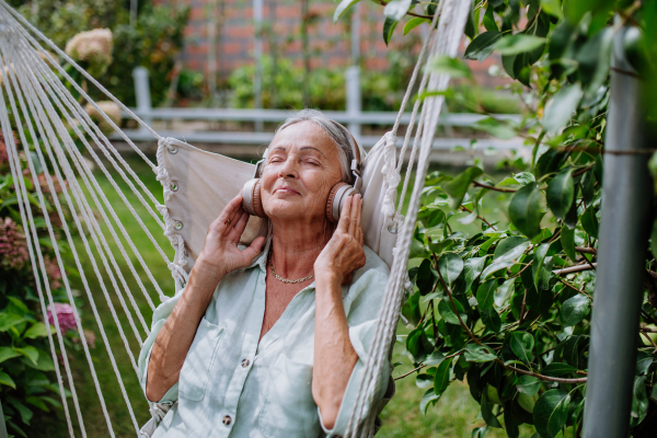 Senior woman relaxing in garden swing,listening the music trough headphones.