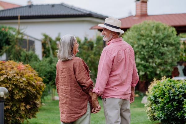 Rear view of senior couple posing together in the garden, holding each other hands.