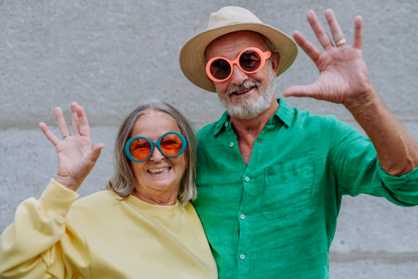 Portrait of happy seniors couple in a colourful clothes waving at camera.