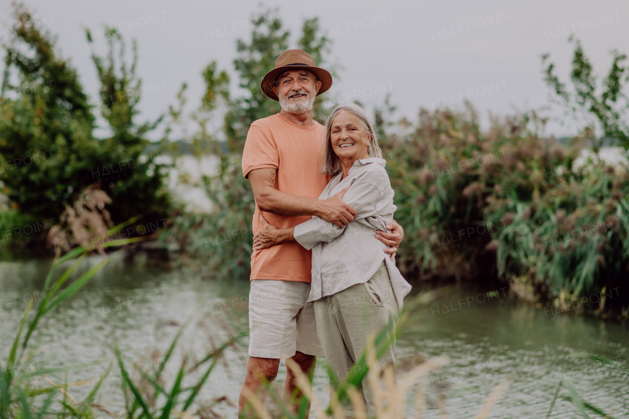 Happy senior couple hugging on walk near the lake during cloudy autumn day.