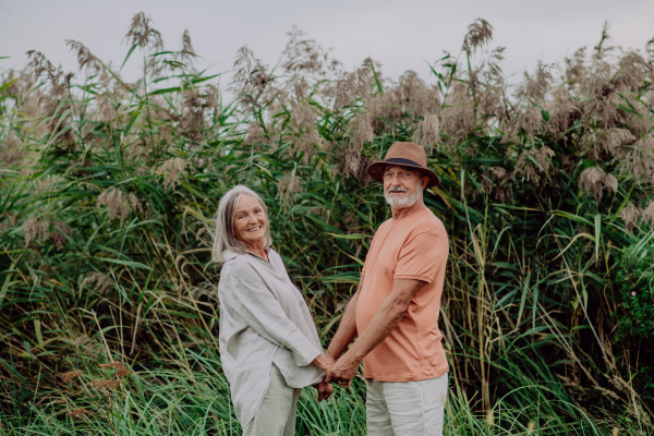 Happy senior couple on walk near the lake during cloudy autumn day.