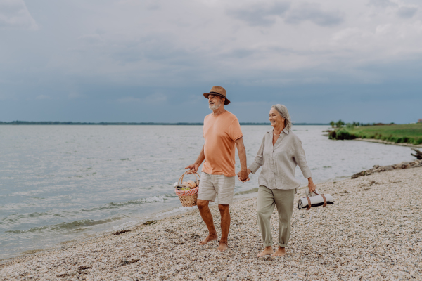 Senior couple walking with picnic basket near the sea.