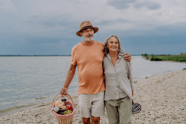 Senior couple walking with picnic basket near the sea.