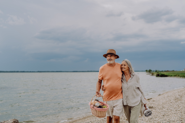 Senior couple walking with picnic basket near the sea.