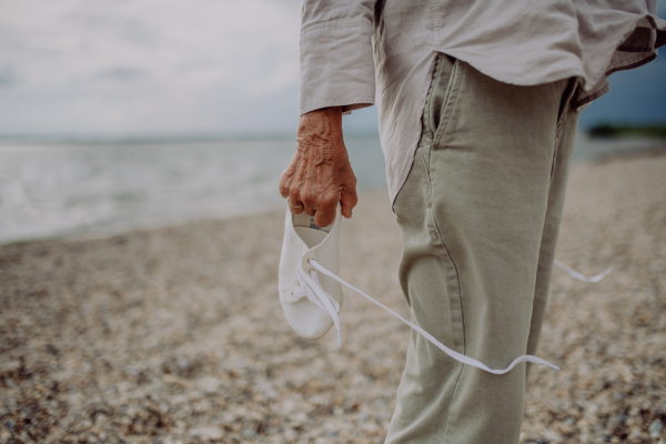 Low section of senior woman standing at a beach with taking off shoes.