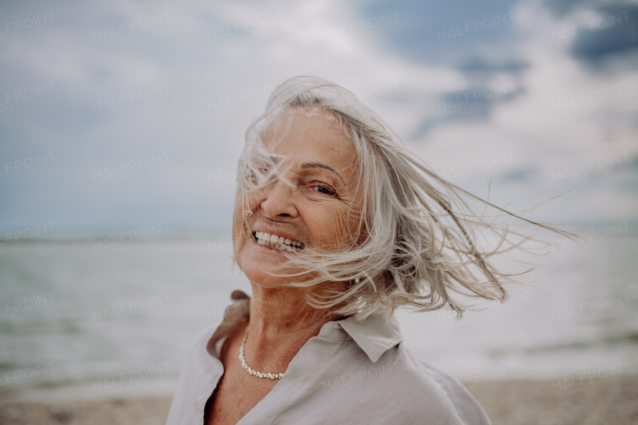 Portrait of happy senior woman with wind in hair, near autumn sea.