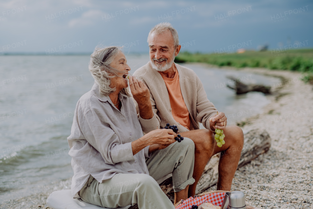 Senior couple sitting and having romantic moment at the autumn sea,eating grape.