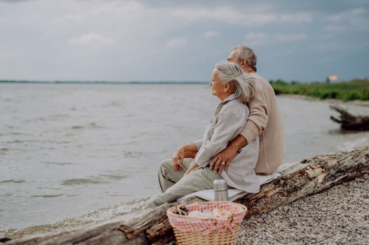 Senior couple sitting with picnic basket, relaxing and having romantic moment at the autumn sea.