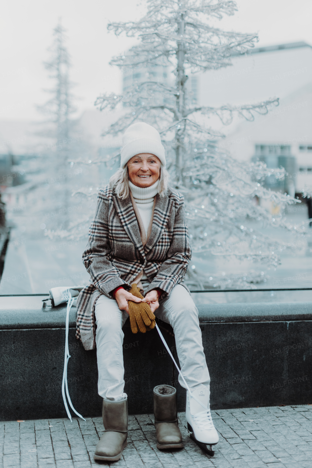 Senior woman sitting at christmas ice rinke in the city and puttion on white ice skates. Learning to skate in old age.