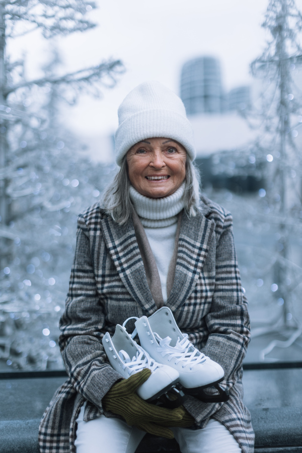 Portrait of happy senior woman in winter at an outdoor ice skating rink. Elderly woman holding brand new ice skates.