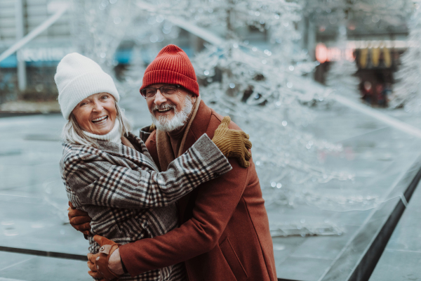 Portrait of seniors in winter at outdoor ice skating rink. Smiling, embracing each other.