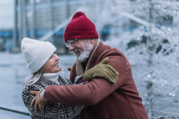 Portrait of seniors in winter at outdoor ice skating rink. Smiling, embracing and looking at each other.