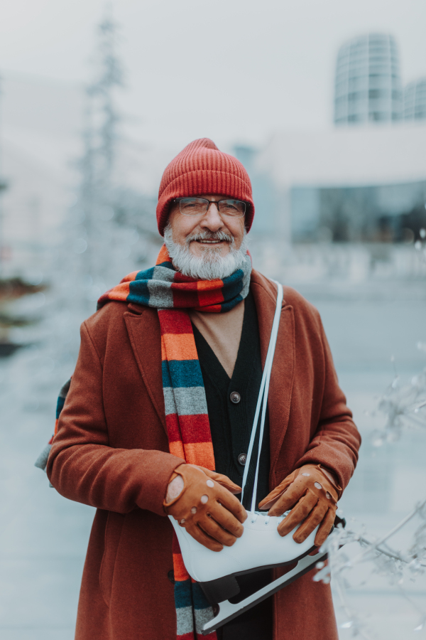 Portrait of happy senior man in winter at an outdoor ice skating rink. Elderly man holding brand new ice skates.