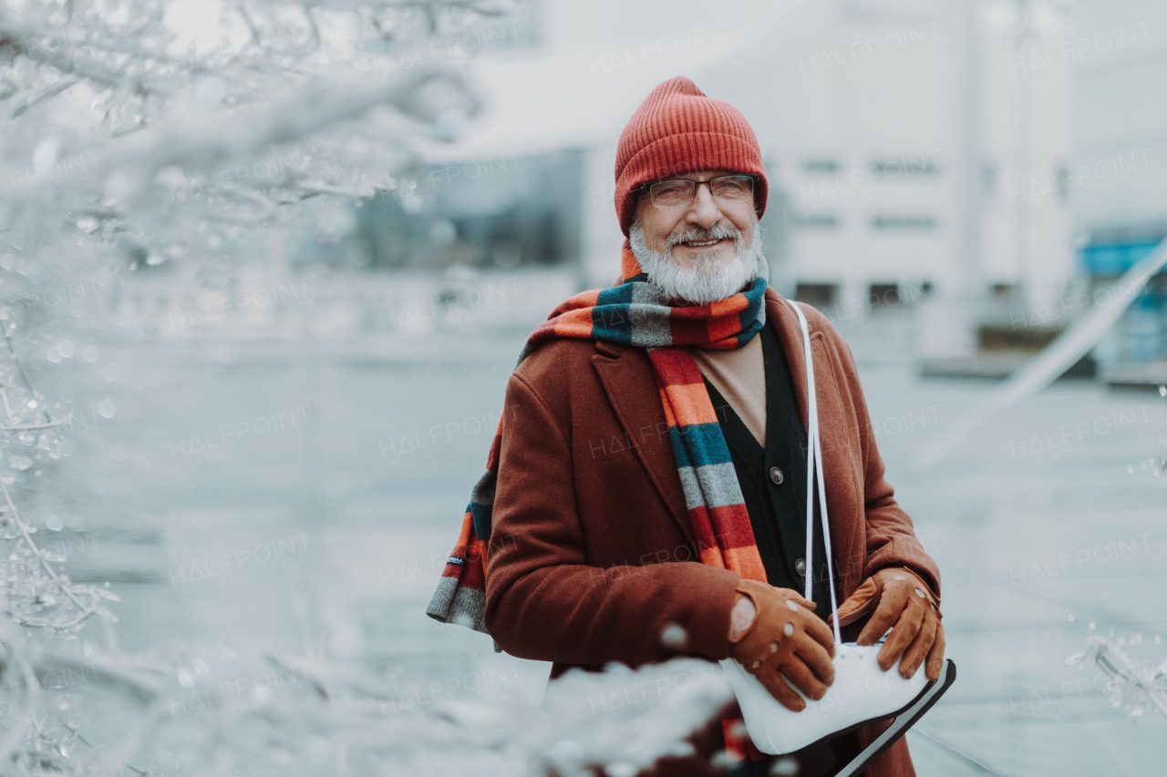 Portrait of happy senior man in winter at an outdoor ice skating rink. Elderly man holding brand new ice skates.