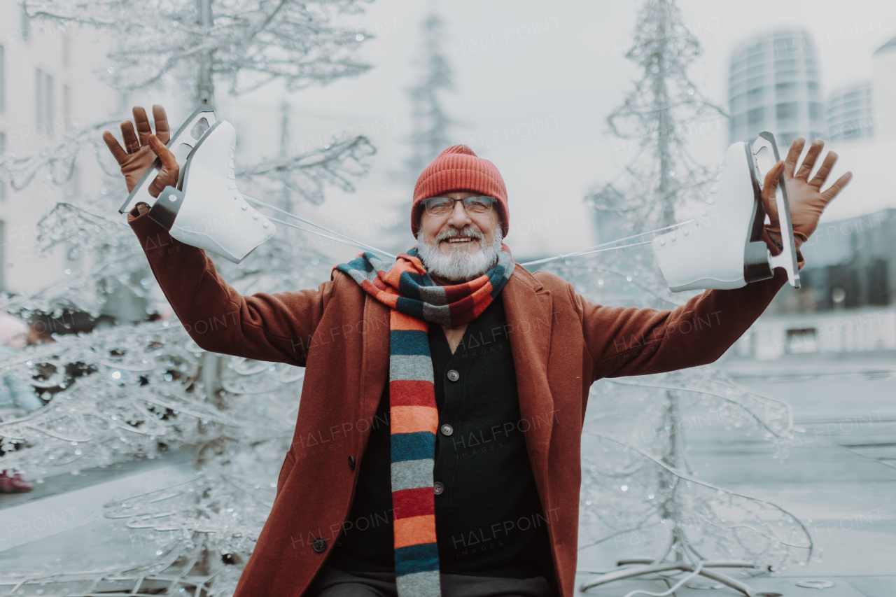 Portrait of senior man at outdoor ice skating rink. Handsome elderly man holding new ice skates.