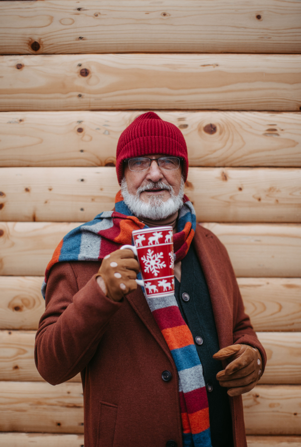 Happy senior man enjoying outdoor christmas market, driking muled wine.