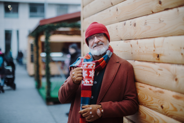 Happy senior man enjoying outdoor christmas market, drinking punch.