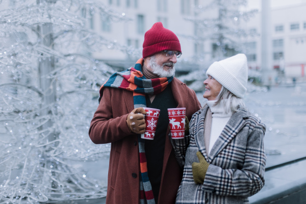 Happy senior couple enjoying outdoor christmas market, driking muled wine.