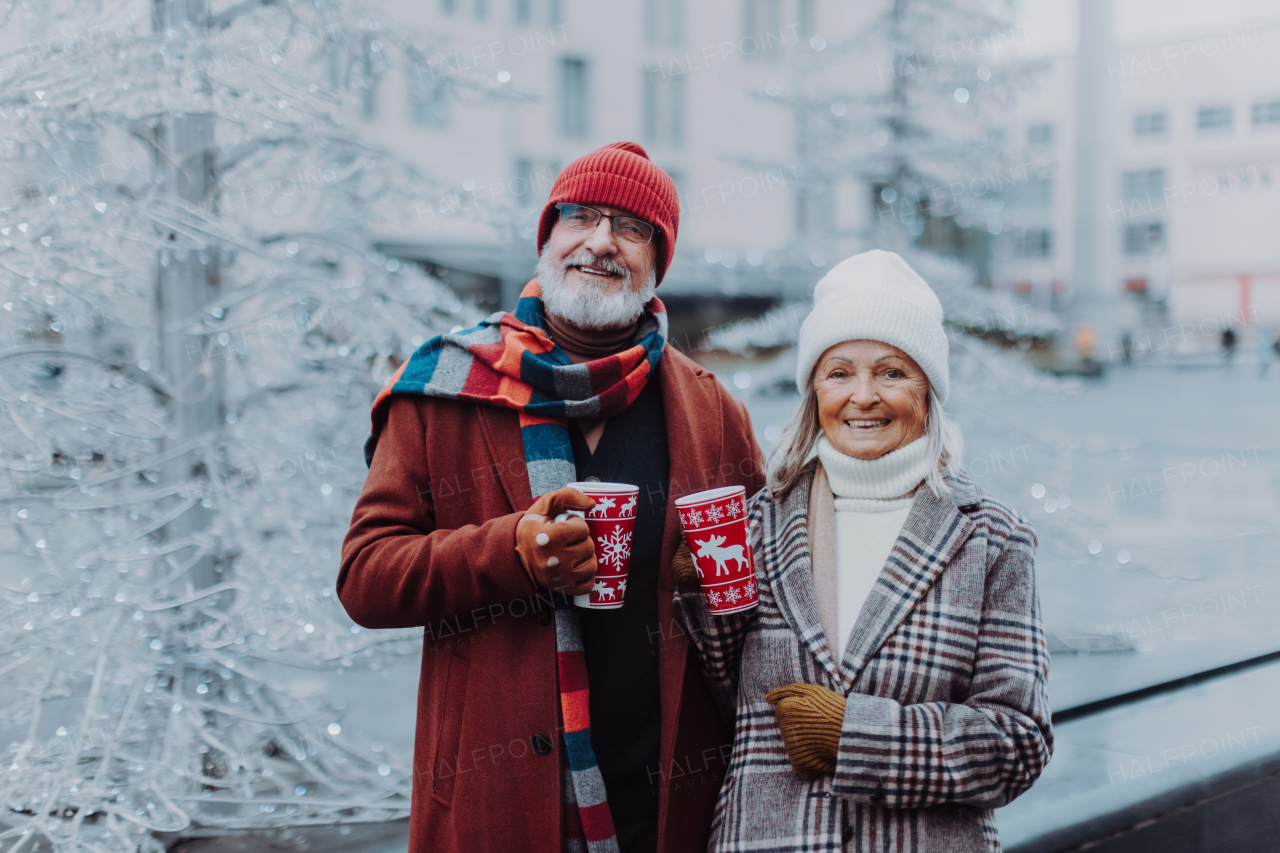 Happy senior couple enjoying outdoor christmas market, driking muled wine.