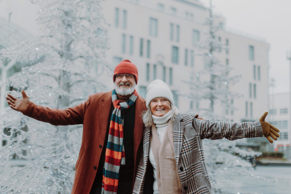 Elegant senior couple in christmas city during cold winter day. Seniors stading with open arms.