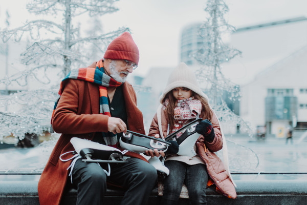 Grandfather with granddaughter in a winter at outdoor ice skating rink. Grandparents teaching cute girl how to ice skating.